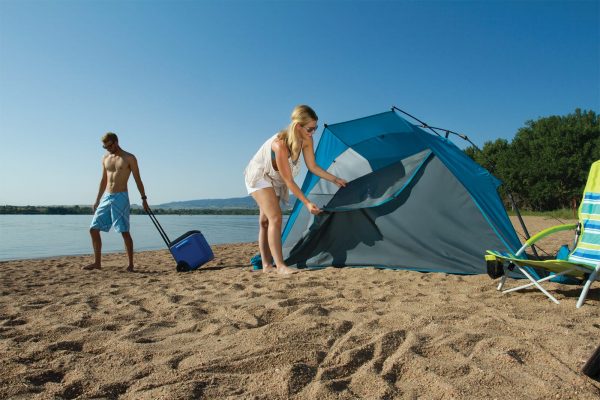 A woman setting up a tent on the beach while her boyfriend is pulling an ice cooler